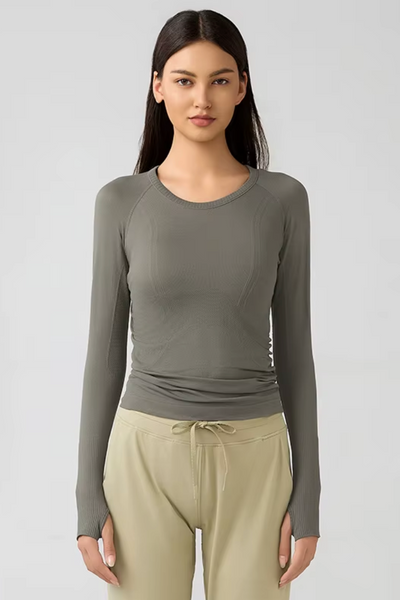 Woman wearing a green long-sleeve top and beige pants on a white background